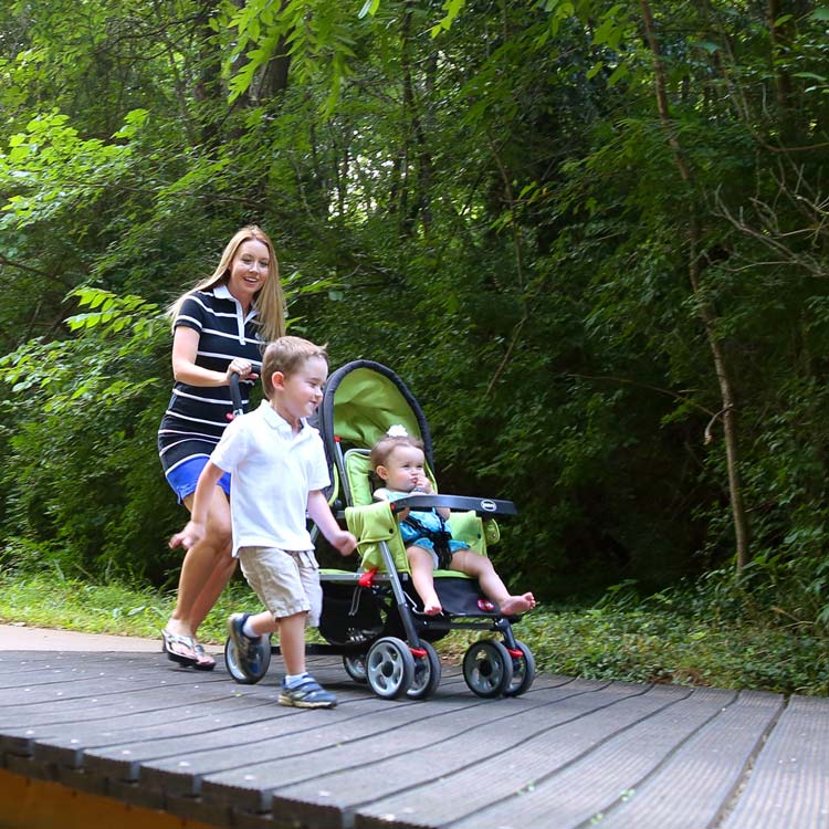 Mother with two kids, one in a stroller, walking along a paved trail in the woods