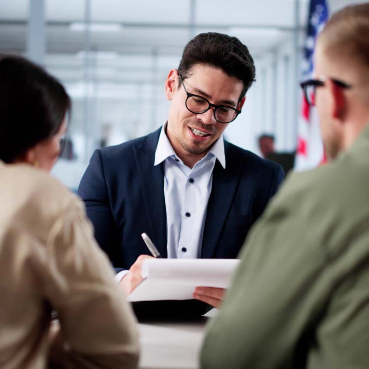 Professionally dressed man making notes on a pad of paper while talking to two others