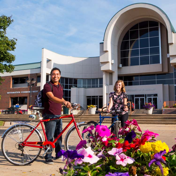 Man and woman standing with bikes in front of a building on the Ozarks Tech campus