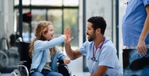 Medical professional kneeling, high-fiving young patient in a wheelchair