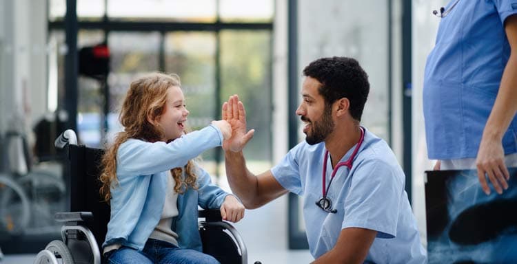 Medical professional kneeling, high-fiving young patient in a wheelchair