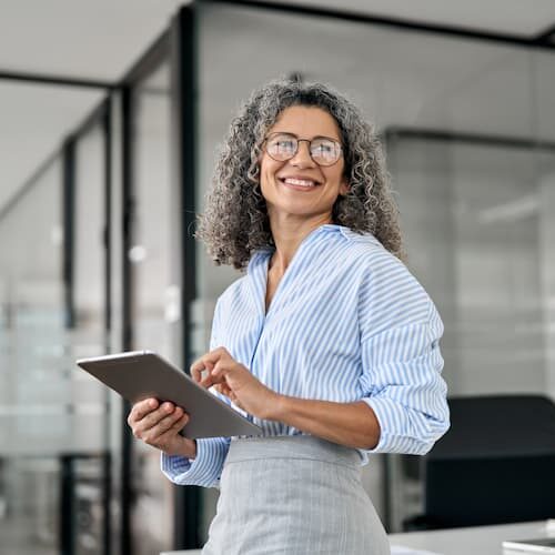 Professional woman in an office, smiling and holding a digital tablet