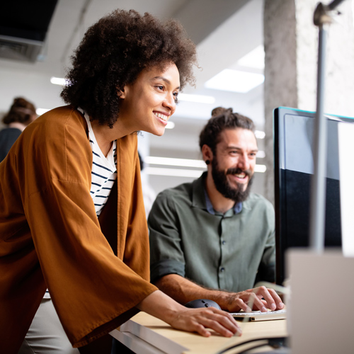 Two professionals looking toward a computer screen, both smiling